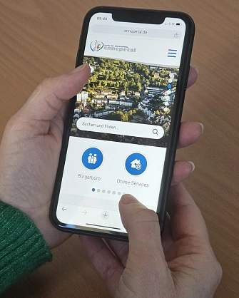 Homepage_mobil_komp.jpg Hand hält Smartphone, auf dem die neue Webseite der Stadt zu sehen ist.